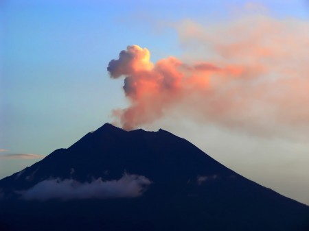 The red light of sunset lights up the eruption of Manam Island volcano